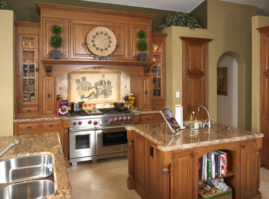 Warm kitchen with wood cabinets, granite island, stainless stove, and arched doorway to the right.