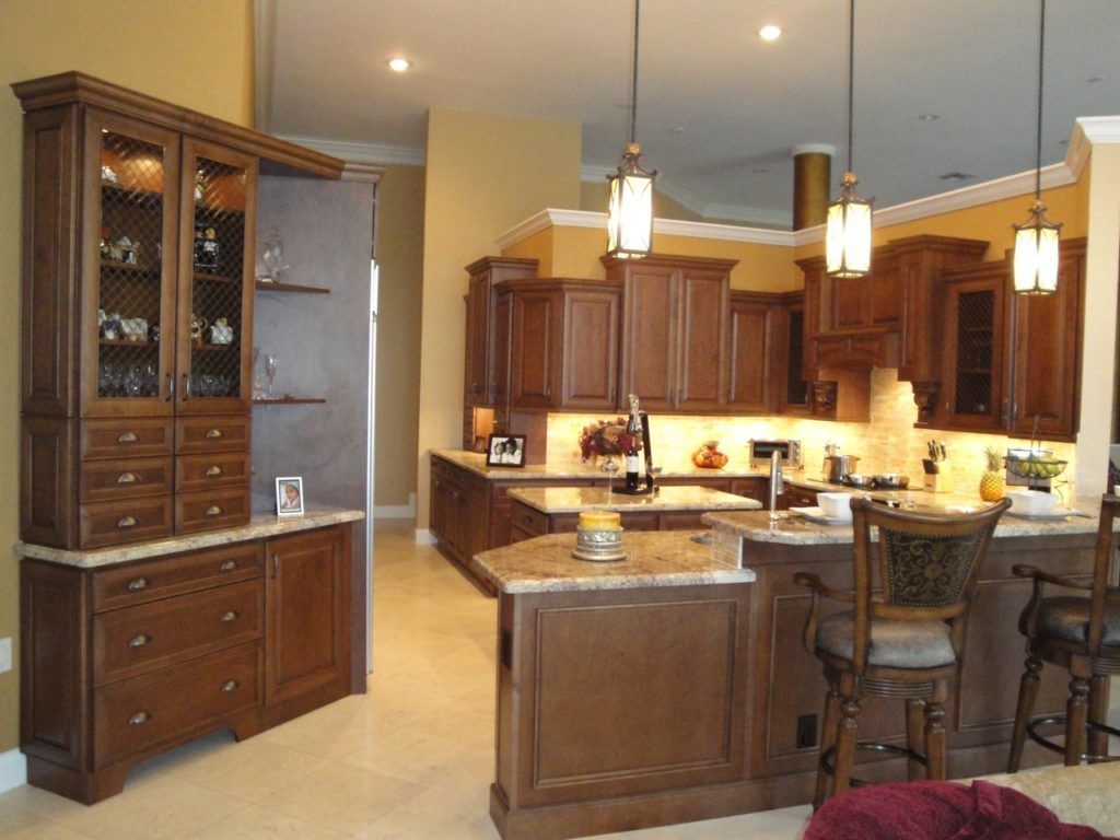 Warm-toned kitchen with wood cabinets, granite island, pendant lights, and a breakfast bar