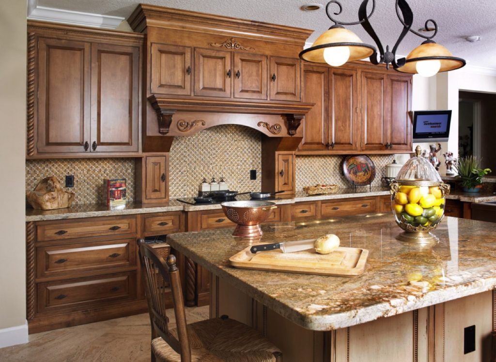 Warm-toned kitchen with wooden cabinets, granite island, tiled backsplash, and a fruit bowl centerpiece.