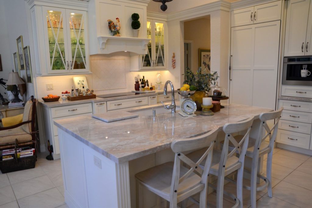 Bright white kitchen with marble island, bar stools, built-in ovens, and warm under-cabinet lighting