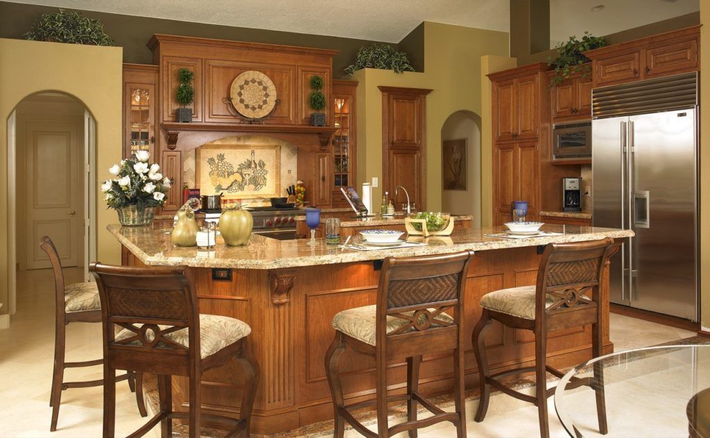 Warm kitchen with wooden island, bar stools, stainless fridge, and neatly set dining counter.