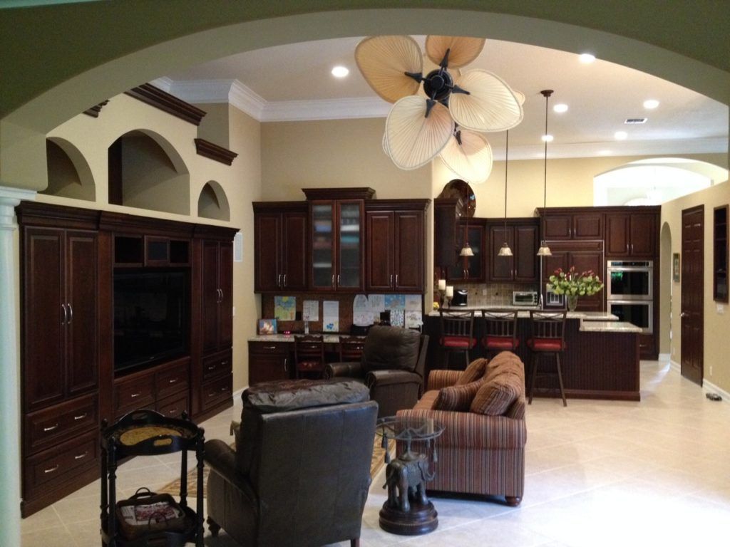 Spacious living room with dark wood cabinets, brown sofa, chairs, and a large ceiling fan chandelier.