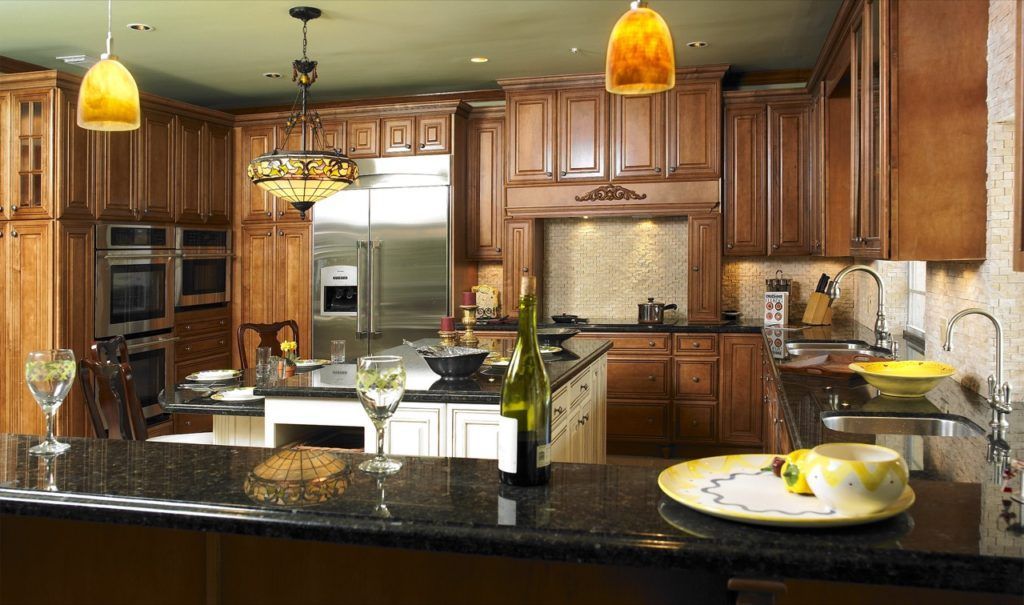 Modern kitchen with wooden cabinets, black granite island, pendant lights, and a dining table set for two.