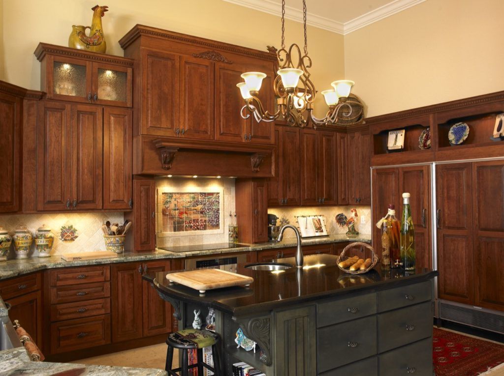 Warm kitchen with dark wood cabinets, black island, hanging lights, and decorative plates on shelves.