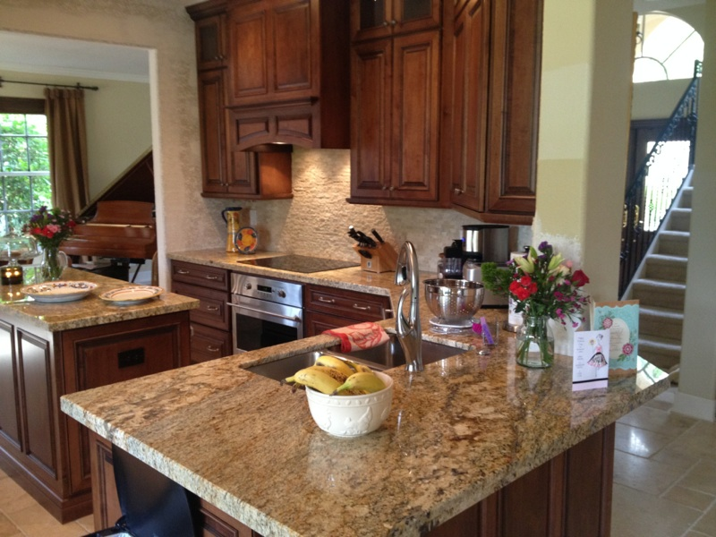 Modern kitchen with granite island, wood cabinets, stainless appliances, and staircase view