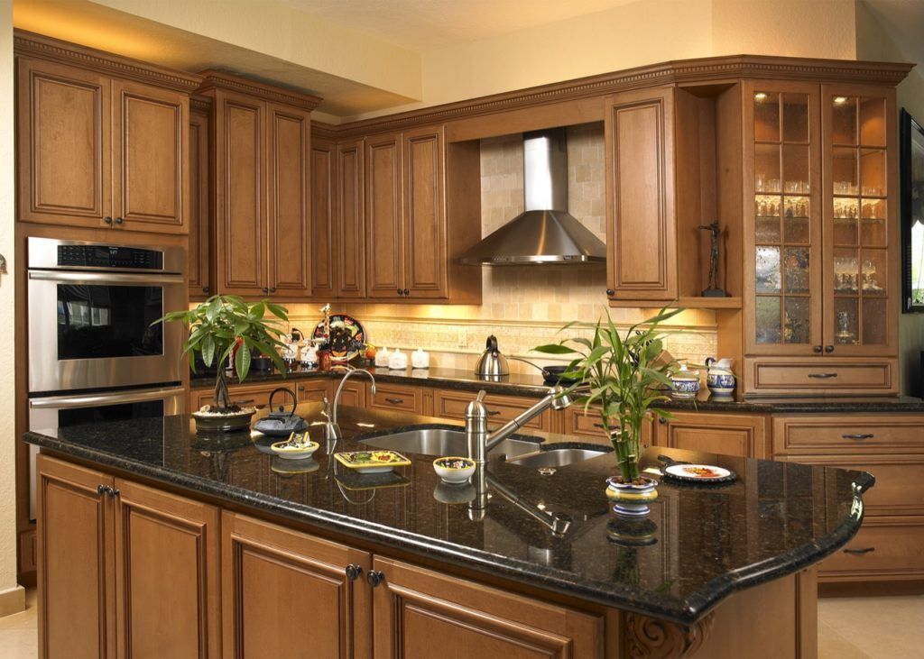 Modern kitchen with wooden cabinets, granite island, stainless steel appliances, and potted plants