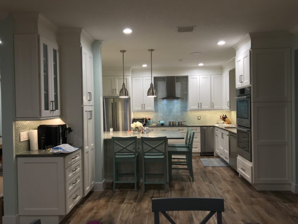 Modern kitchen with white cabinets, stainless steel appliances, and a turquoise island with barstools.