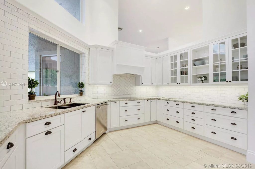Bright white modern kitchen with marble counters, glass-front cabinets, and large windows