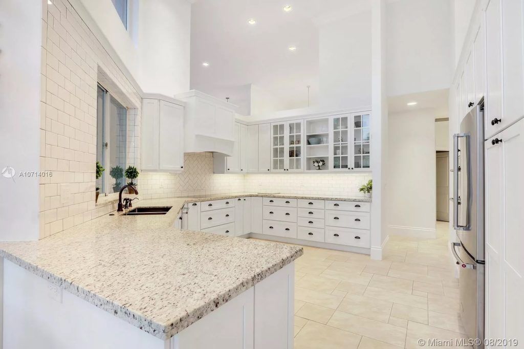 Bright white modern kitchen with marble island, cabinets, and stainless steel appliances