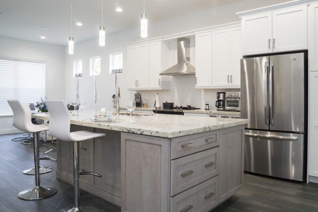 Bright modern kitchen with white cabinets, granite island, bar stools, and stainless steel fridge