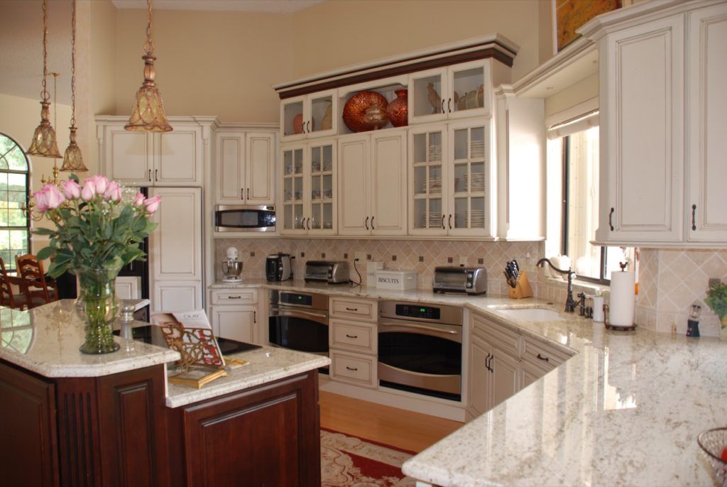 Bright luxury kitchen with white cabinets, marble counters, and a flower arrangement on the island.