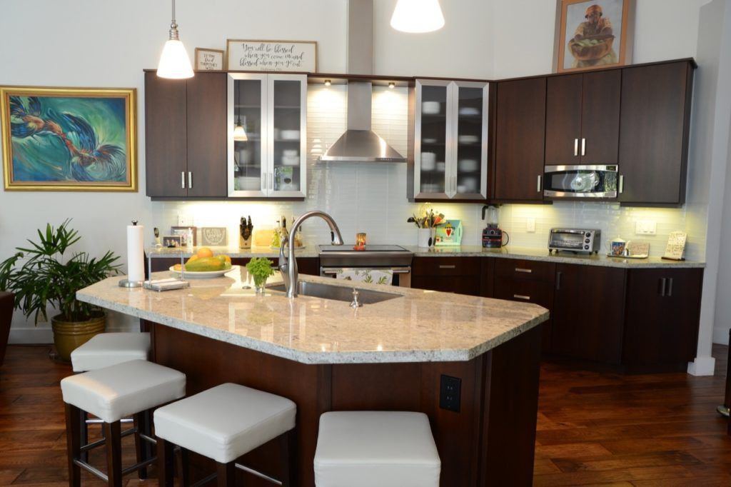 Modern kitchen with granite island, dark cabinets, pendant lights, and three white stools