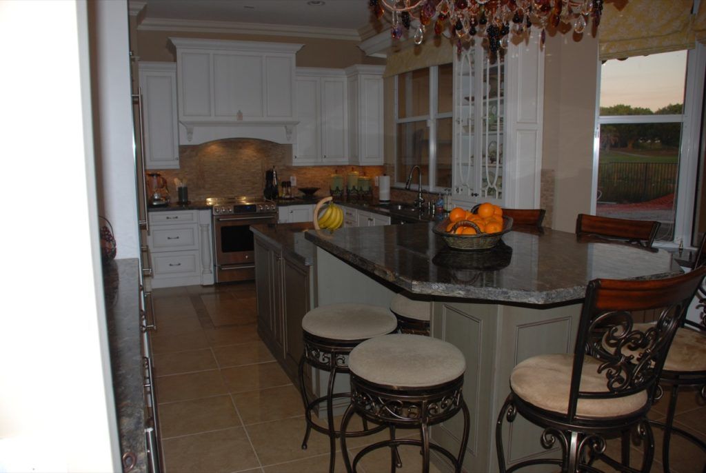 Modern kitchen with granite island, white cabinets, bar stools, and fruit on the counter