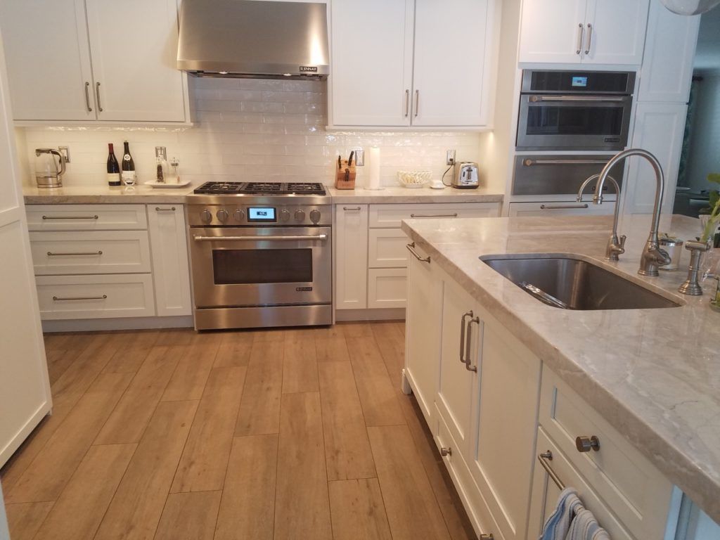 Modern white kitchen with stainless steel appliances, island sink, and wood floor