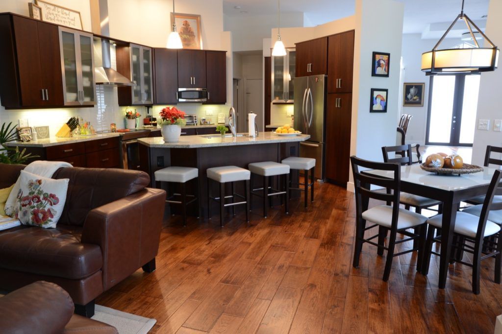 Open-concept kitchen and dining area with dark wood cabinets, island stools, and a brown sofa on hardwood floors