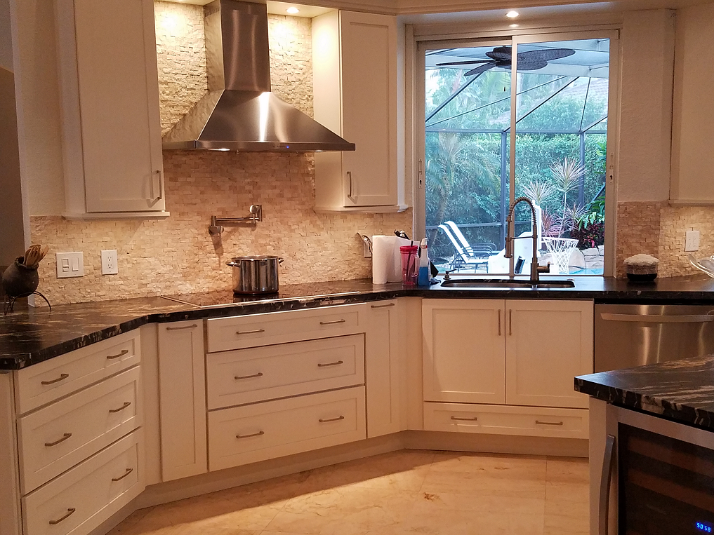 Modern kitchen with white cabinets, granite counters, stainless range hood, and a window over the sink