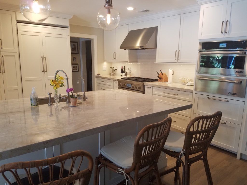 Bright white kitchen with marble island, pendant lights, and wicker bar stools