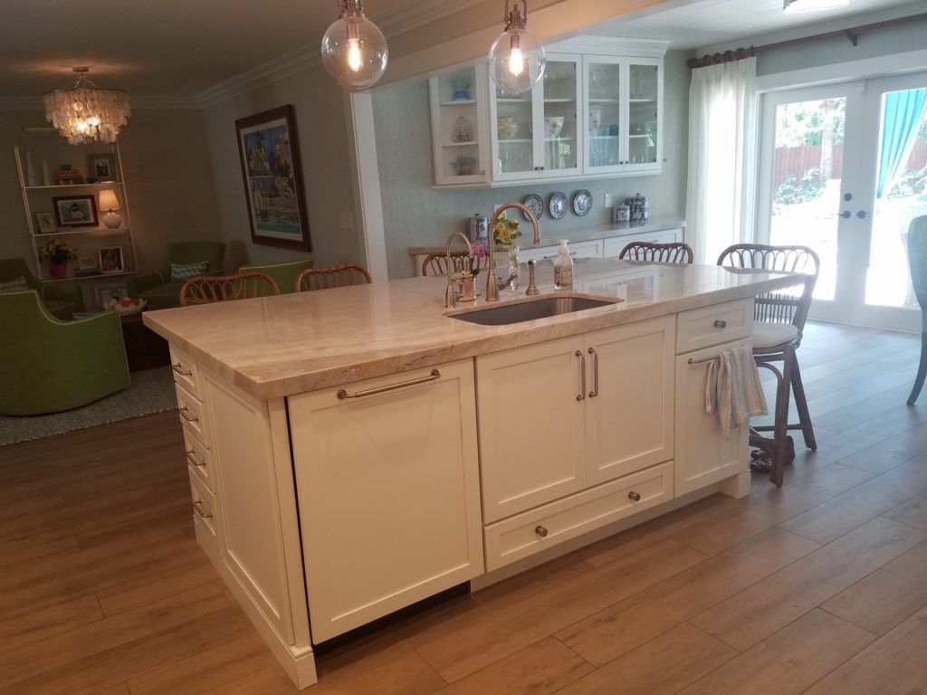 Bright kitchen with a large white island, hanging pendant lights, and an open view to a dining area.