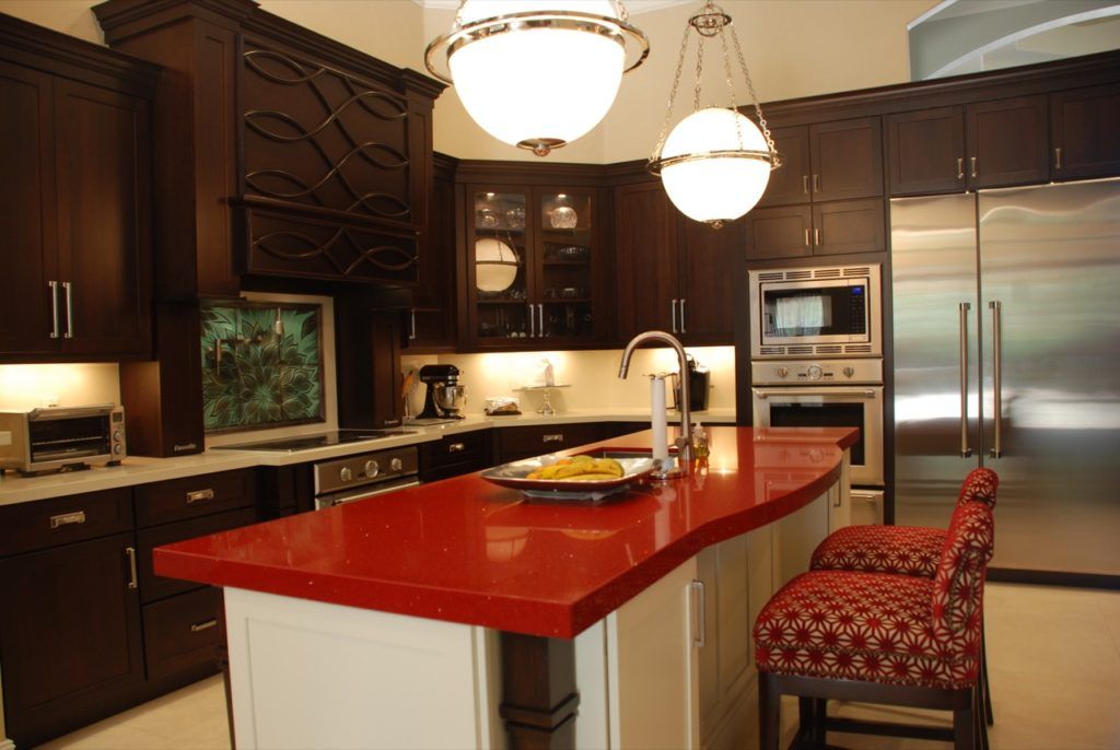 Modern kitchen with dark cabinets, red island countertop, stainless steel appliances, and hanging pendant lights