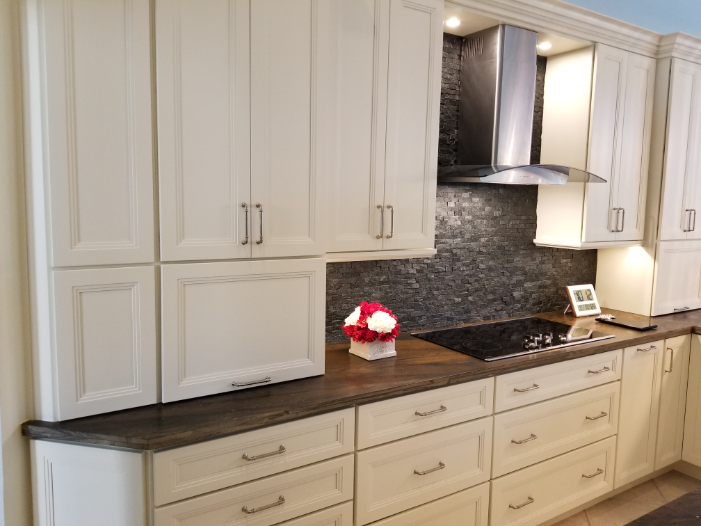 Modern kitchen with white cabinets, dark countertops, tile backsplash, and stainless range hood