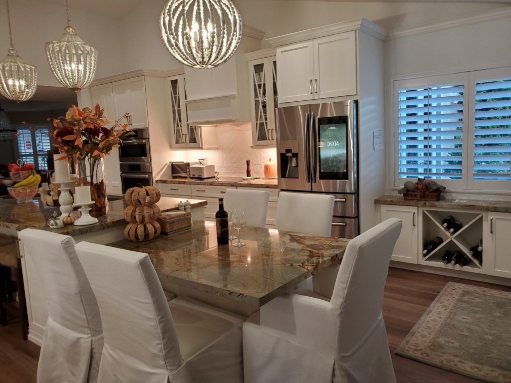 Elegant white kitchen and dining area with a large island, pendant lights, and stainless steel appliances.