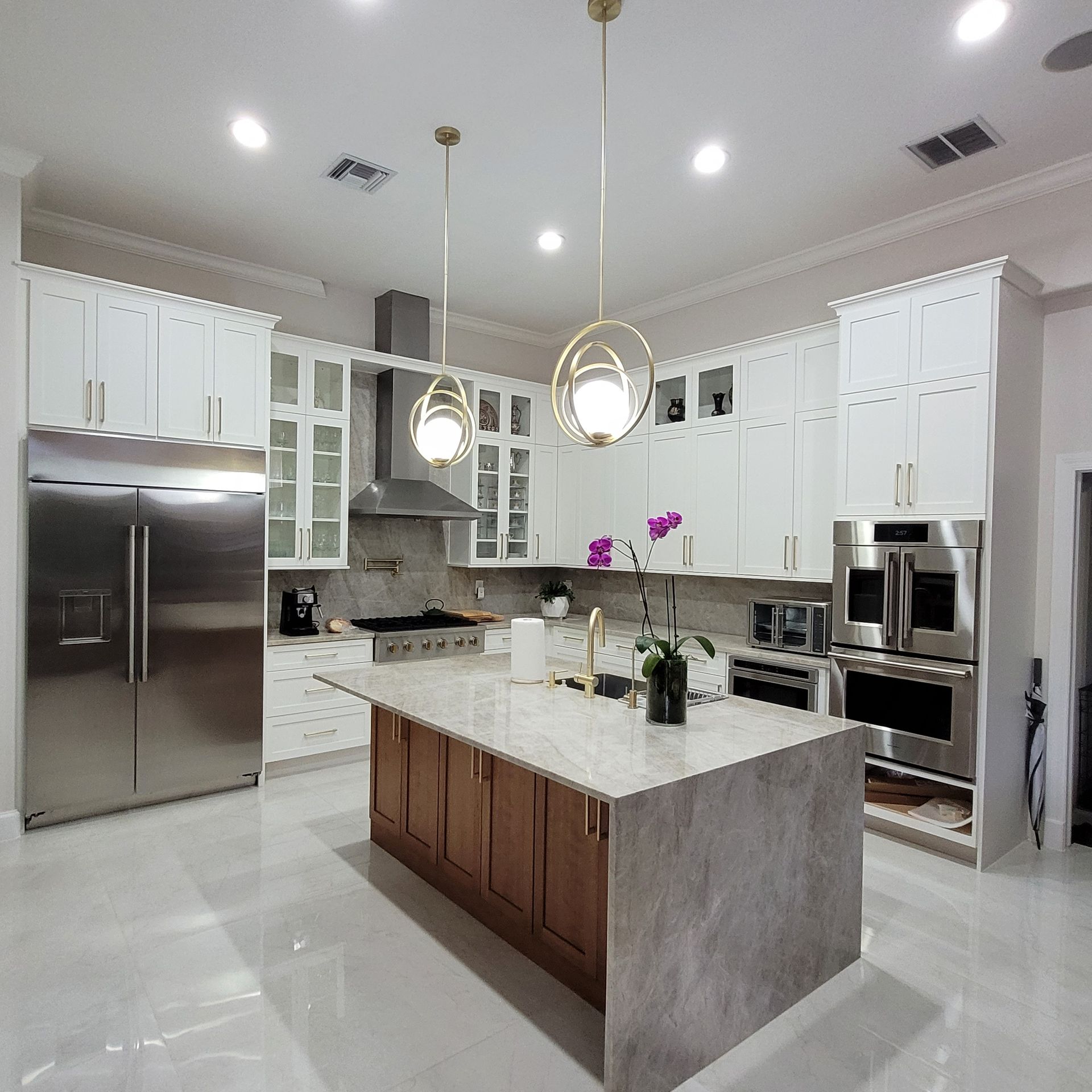 Bright modern kitchen with white cabinets, stainless appliances, and a marble island with gold pendant lights