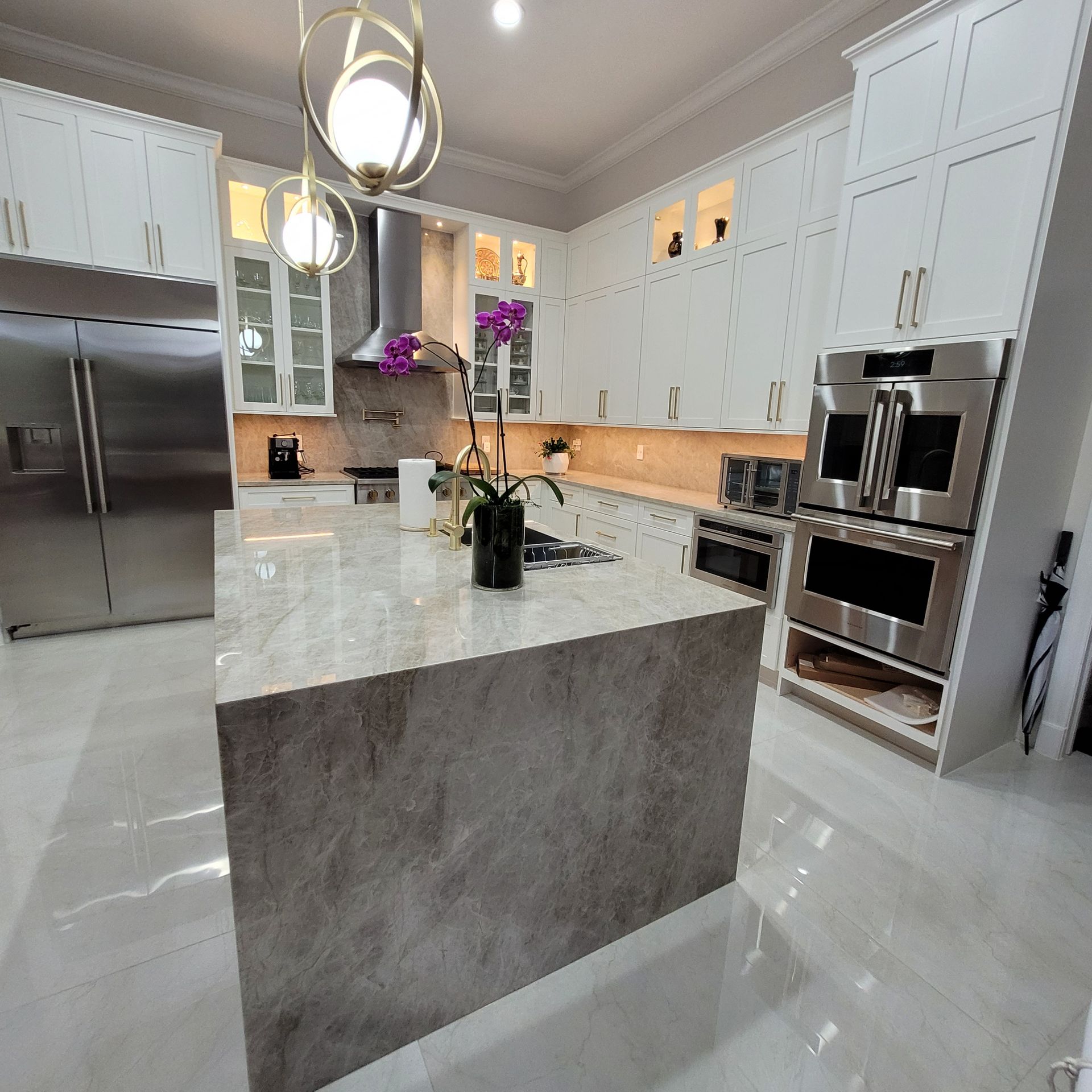 Modern white kitchen with stainless appliances, marble island, and glossy tile floors