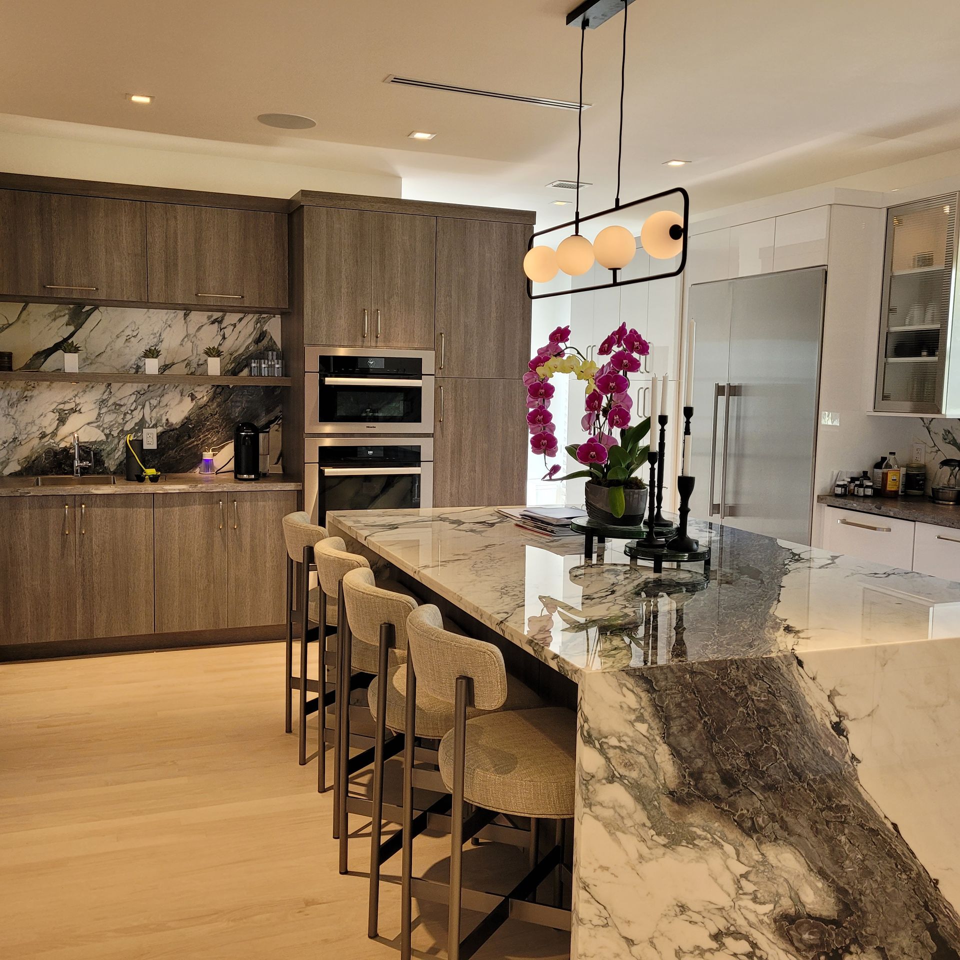 Modern kitchen with marble island, wood cabinets, built-in ovens, and hanging pendant lights
