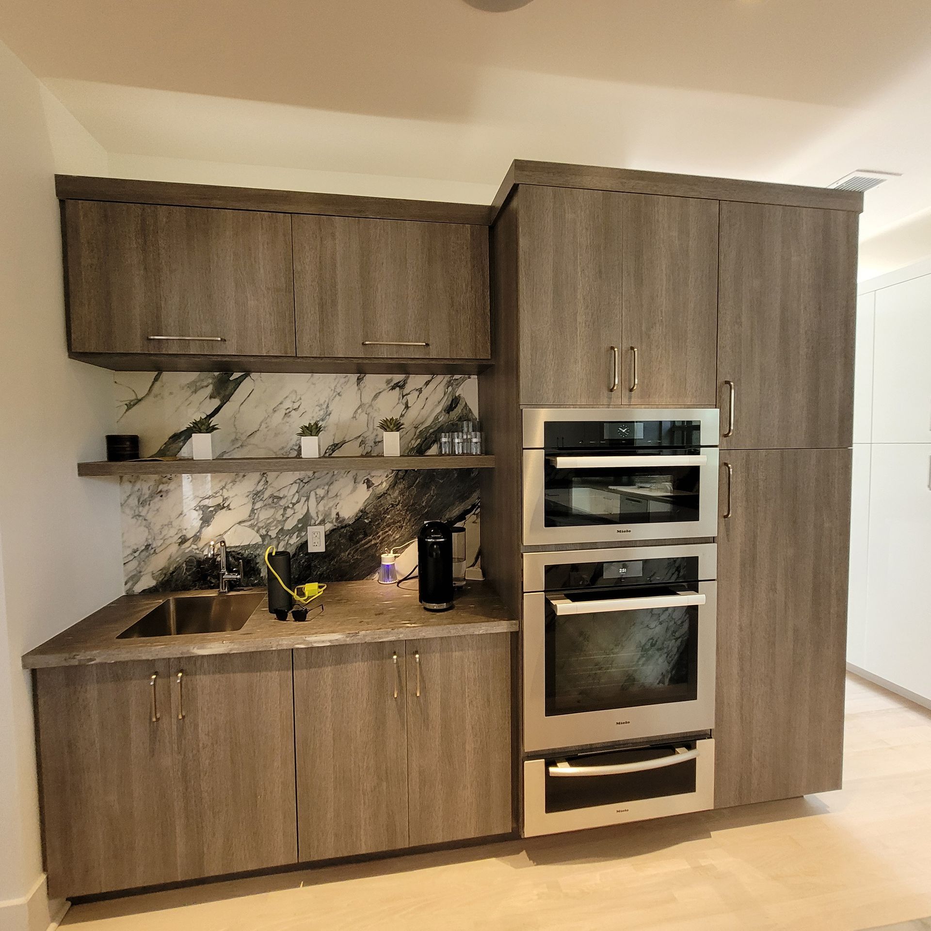 Modern kitchen with wood cabinets, marble-look backsplash, open shelves, and built-in double oven.