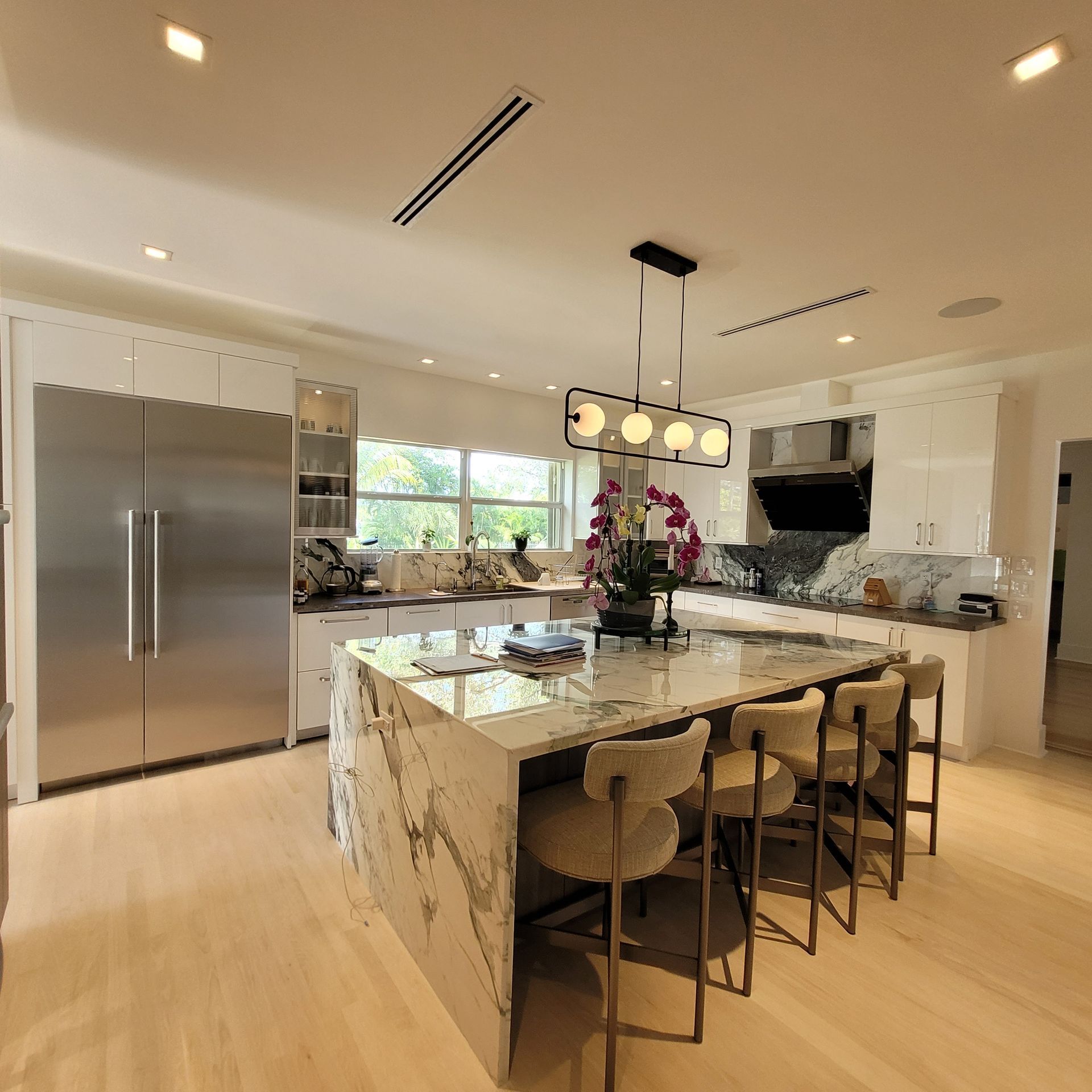 Modern kitchen with marble island, stainless steel fridge, pendant lights, and large window