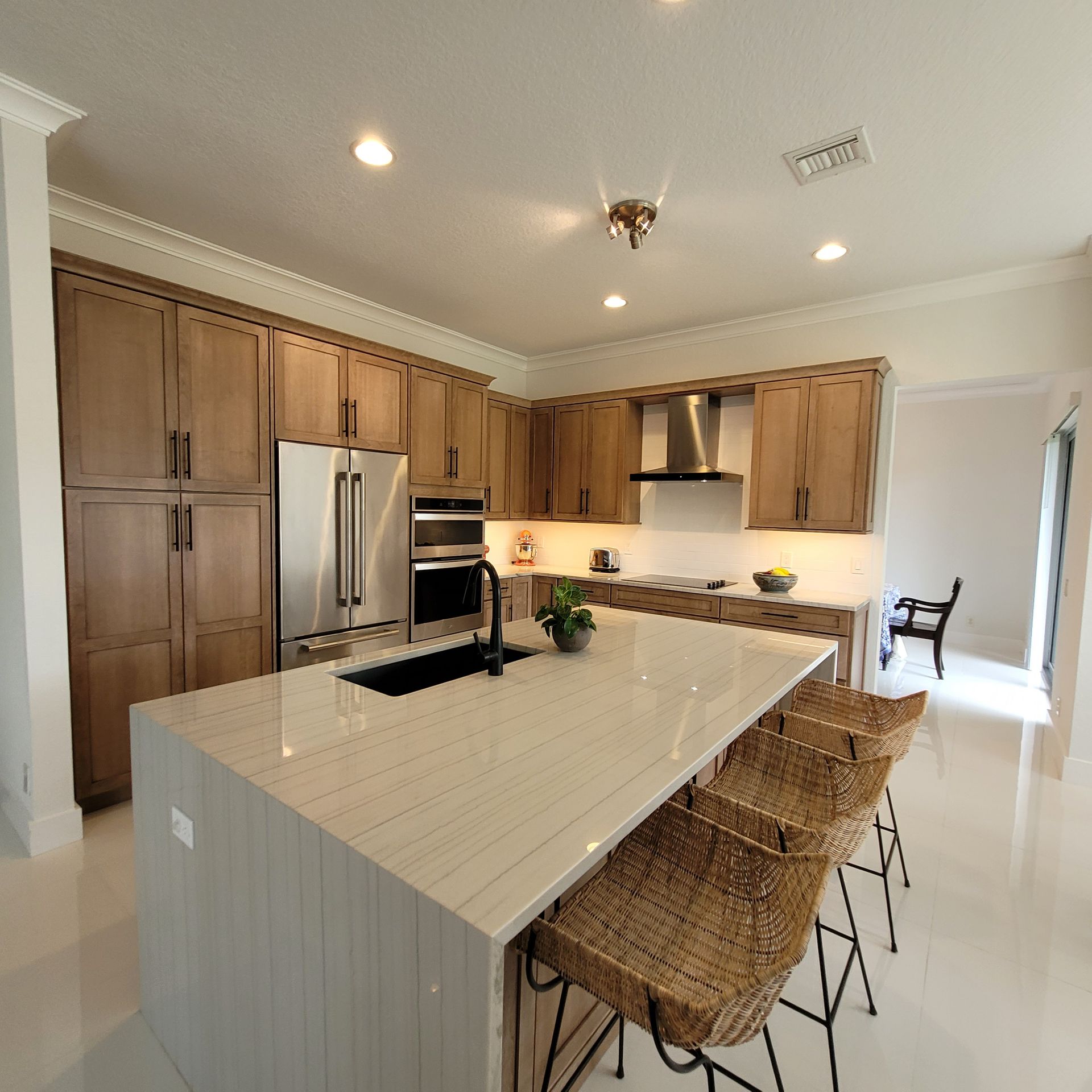 Bright modern kitchen with large island, stainless steel appliances, wood cabinets, and wicker barstools