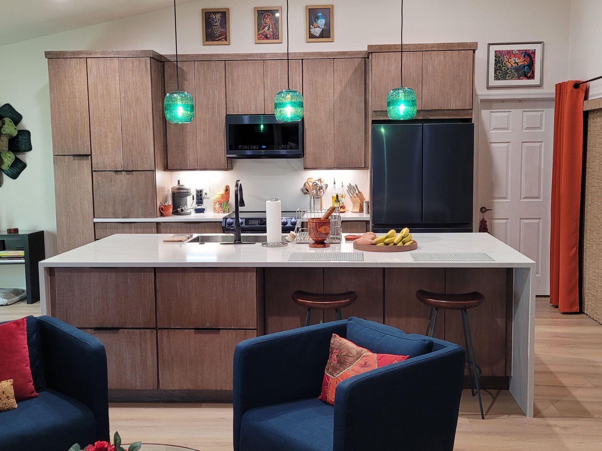 Modern kitchen with wood cabinets, white island, black fridge, and green pendant lights.
