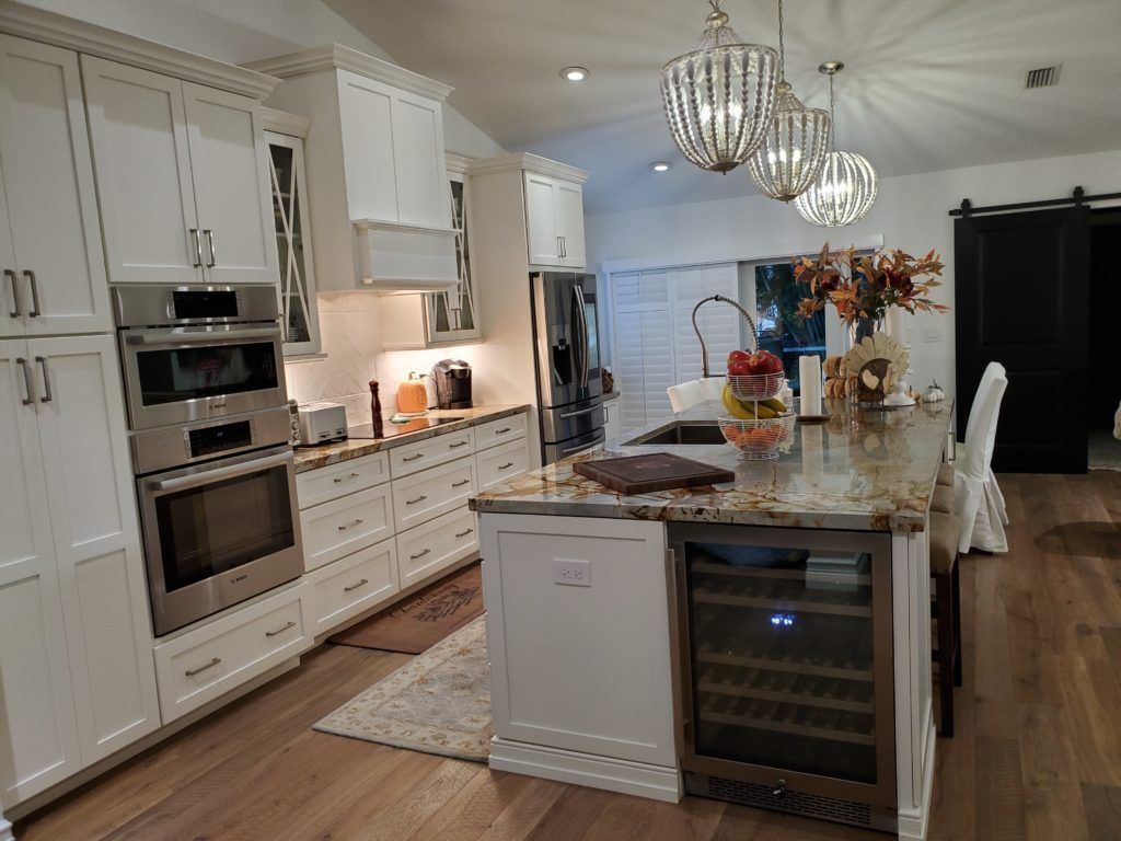 Bright white kitchen with large marble island, pendant lights, double ovens, and wine cooler