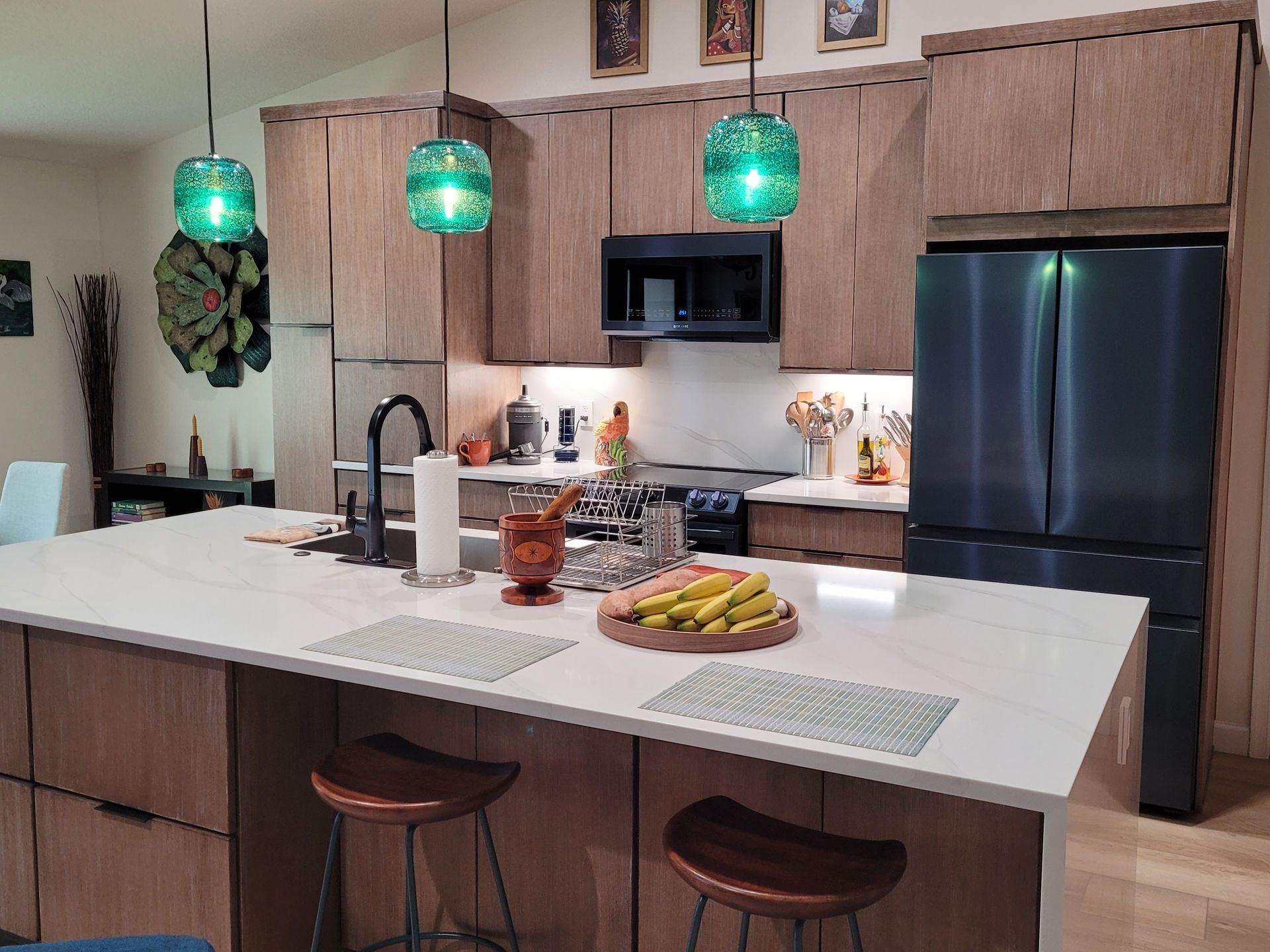Modern kitchen with island, green pendant lights, black appliances, and bowls of fruit on the counter