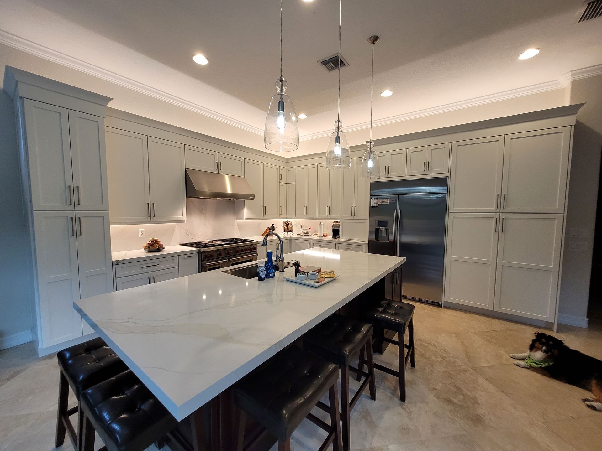 Bright kitchen with a large white island, gray cabinets, pendant lights, and a black refrigerator.