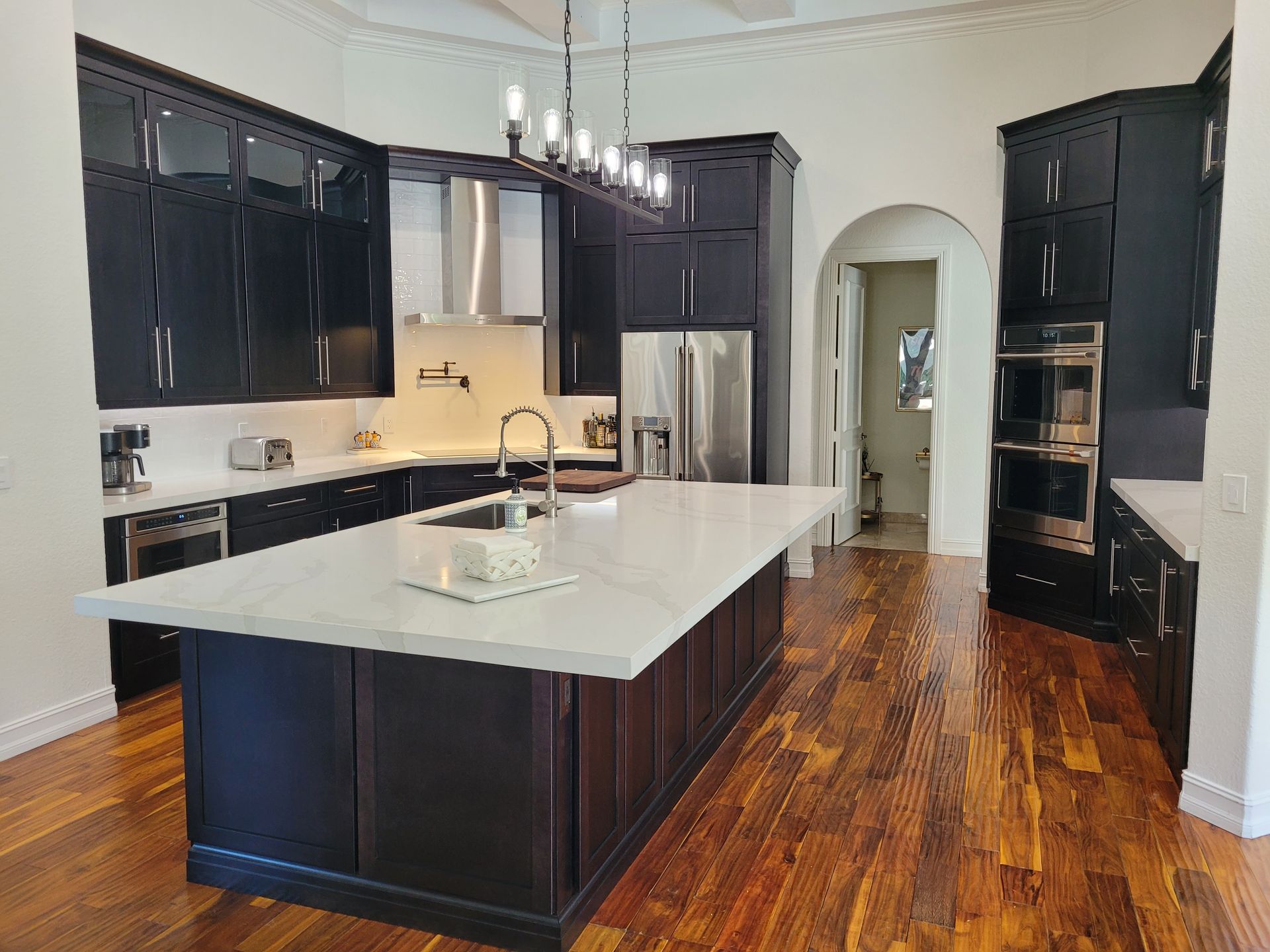 Modern kitchen with dark cabinets, white island, stainless appliances, and hardwood floors