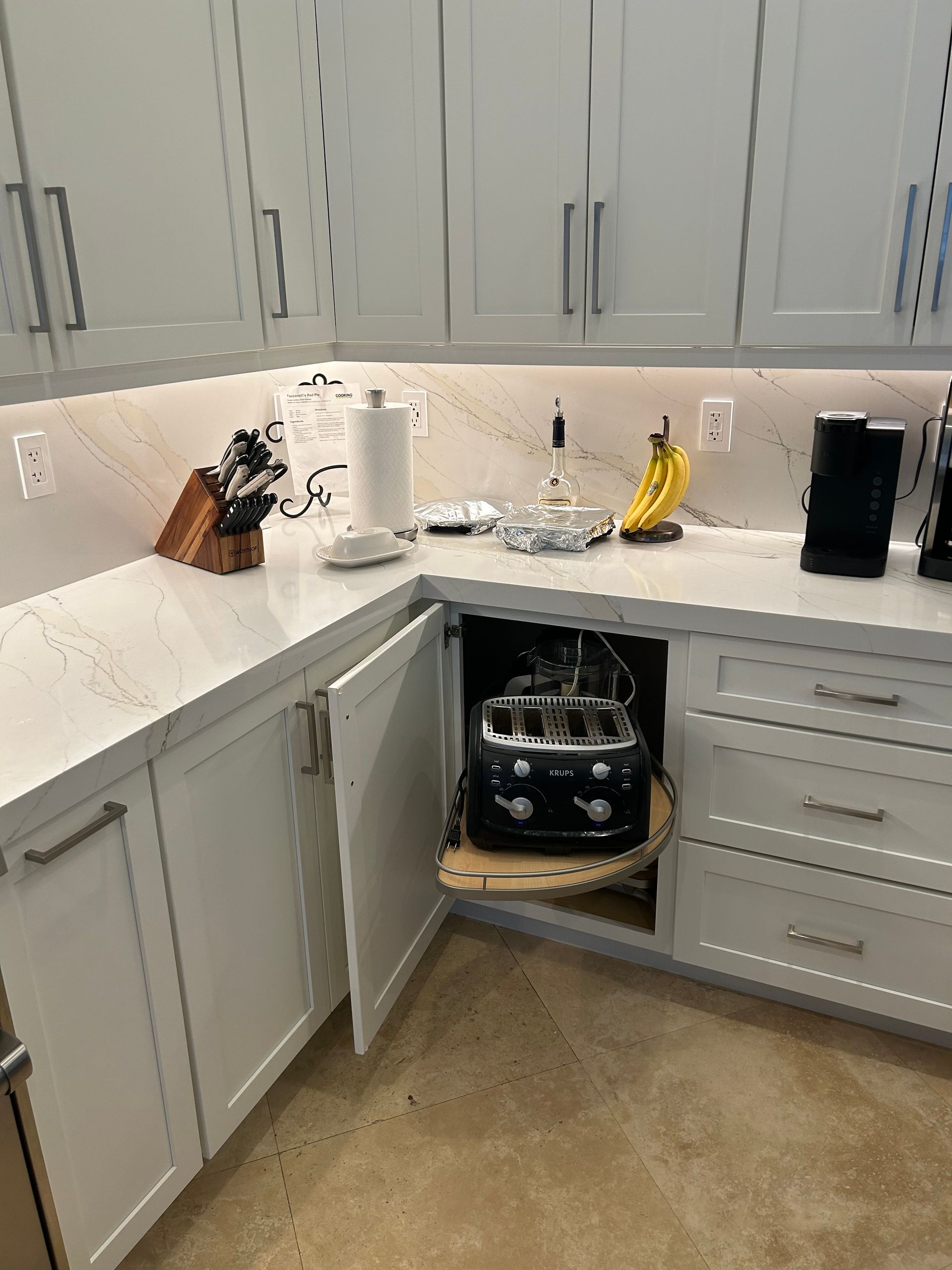 Small kitchen with gray cabinets, white countertops, and an open under-sink cabinet exposing plumbing.