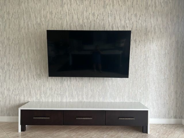 Wall-mounted TV above a low dark cabinet against a textured beige wall.
