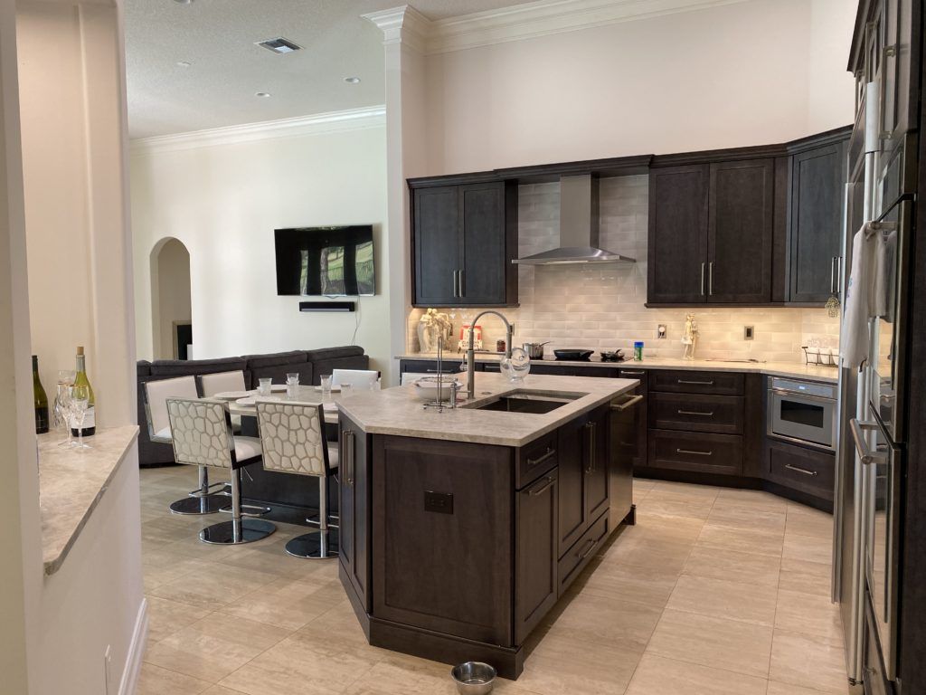 Modern kitchen with dark cabinets, central island, bar stools, and stainless steel appliances.