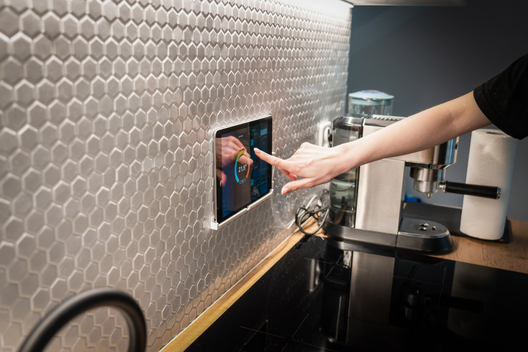 Person touching a wall-mounted touchscreen in a kitchen with hex tile backsplash and countertop appliances