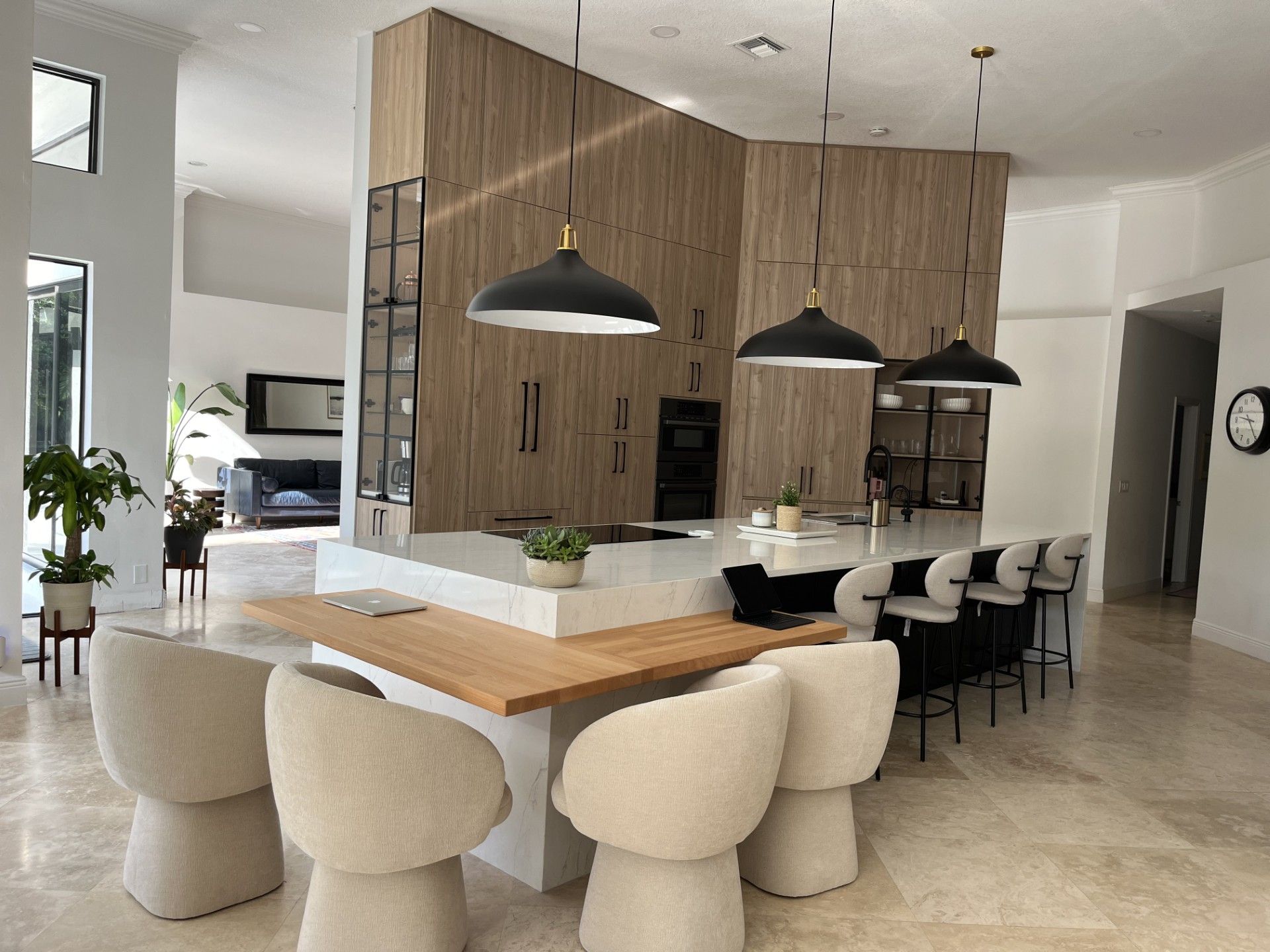 Modern open-plan kitchen with wood island, white bar stools, and black pendant lights