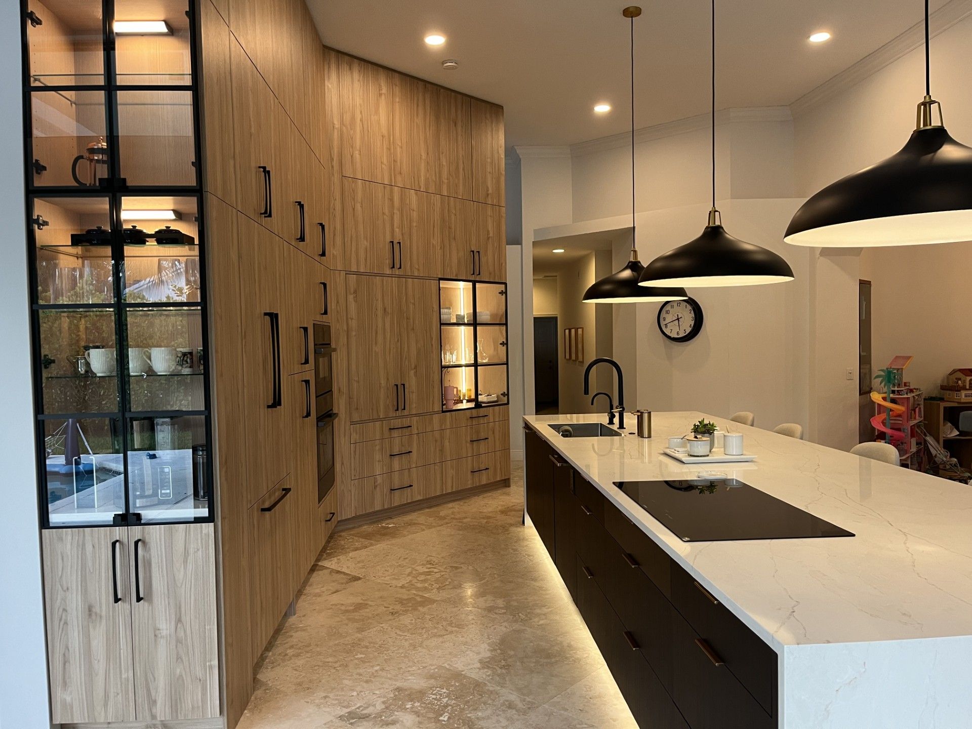 Modern kitchen with wood cabinets, white island, black pendant lights, and large windows