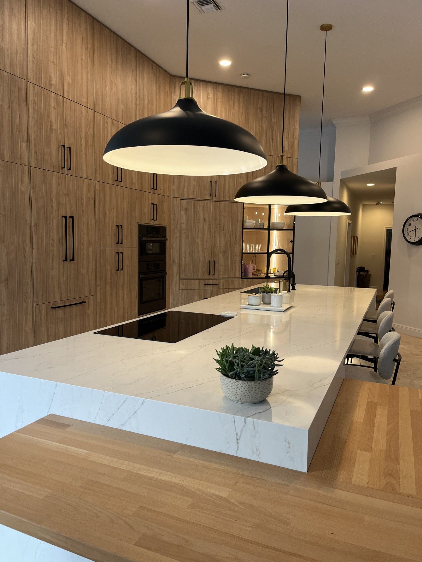 Modern kitchen with wood cabinets, white island, black pendant lights, and bar stools.