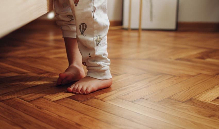 Bare feet in patterned pants standing on a wooden herringbone floor indoors