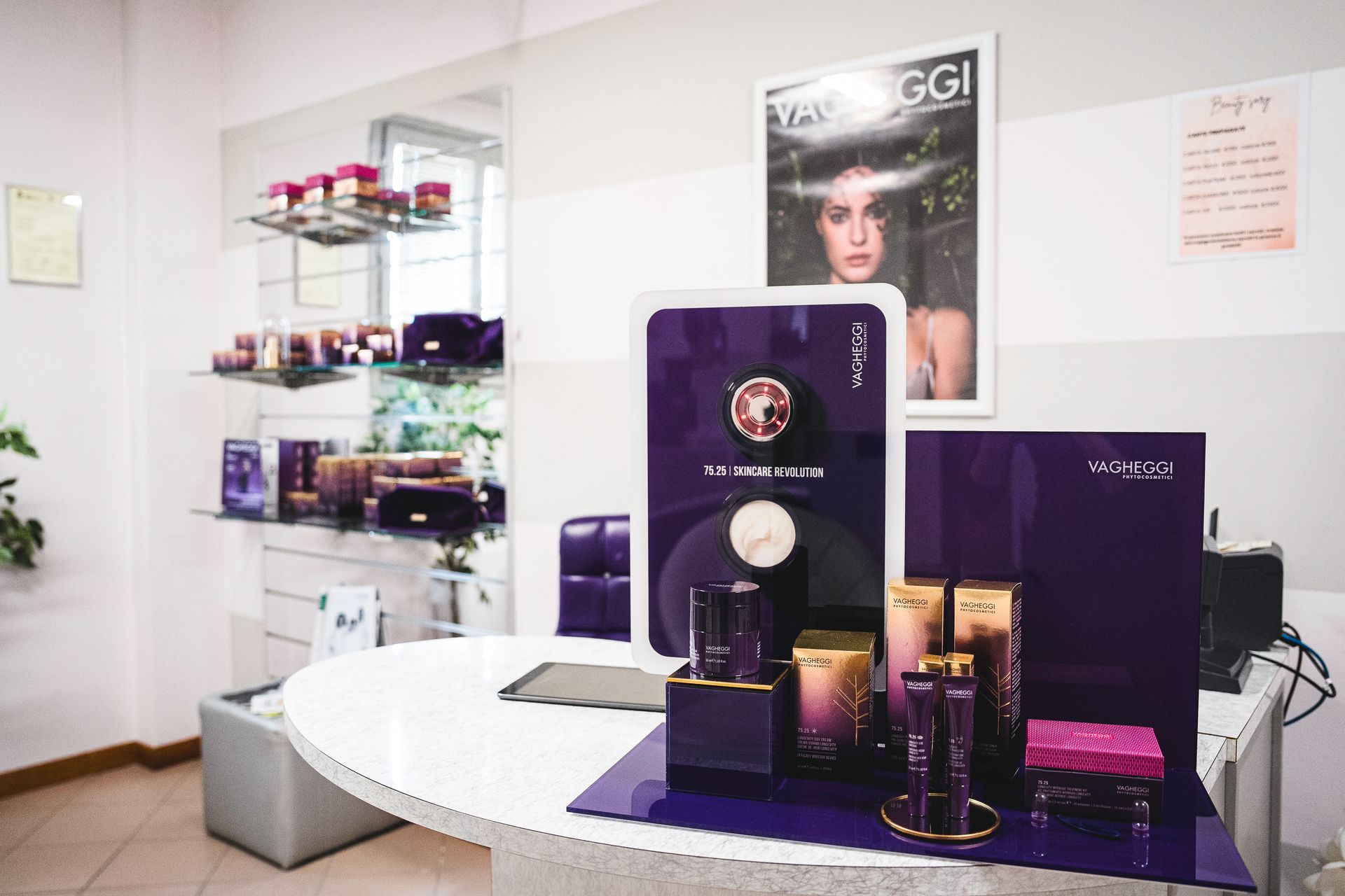 In una boutique ben illuminata, su un bancone bianco, sono esposti prodotti per la cura della pelle nei toni del viola e dell'oro, con un poster del marchio nelle vicinanze.