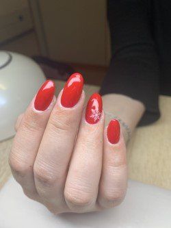 Unghie ovali dipinte di rosso acceso, con un piccolo disegno di un fiocco di neve bianco sull'anulare.