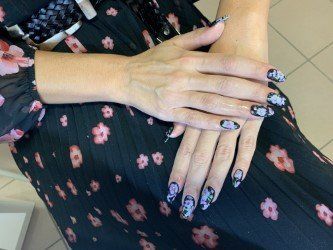 Mani con unghie curate e decorate con motivi floreali poggiavano su un abito nero con una stampa floreale rosa e bianca abbinata.