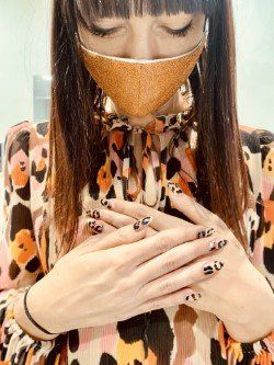 Una persona con lunghi capelli scuri e una maschera dorata indossa un top leopardato con nail art abbinata, con le mani giunte.