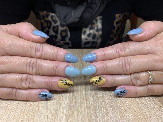 Mani che mostrano unghie a mandorla nei toni del blu polvere e del giallo senape, alcune decorate con delicati motivi a rami neri.