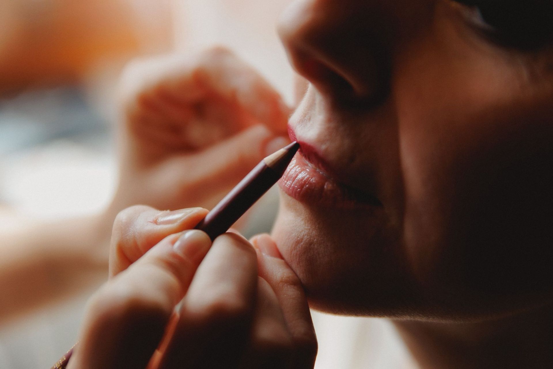 Una persona applica una matita per il trucco sulle labbra di un'altra persona, delineandole con una matita scura.
